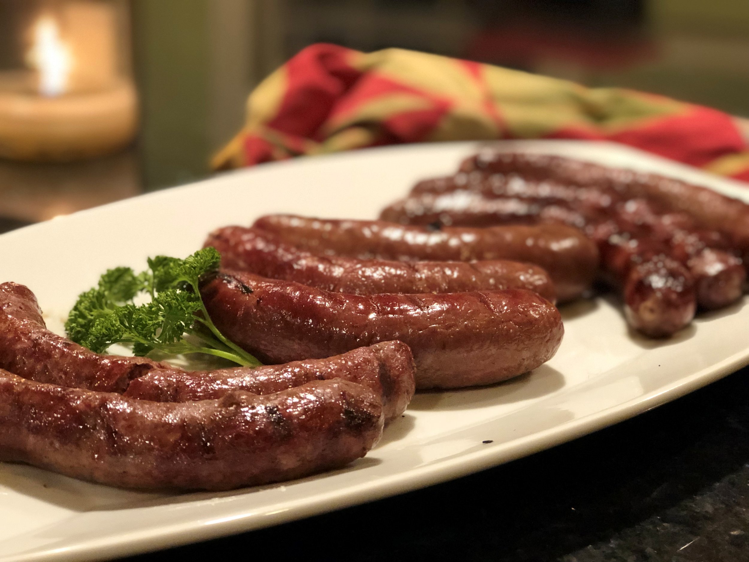 Grilled sausages arranged on a white platter, garnished with fresh parsley, showcasing a variety of textures and colors, ideal for a delicious meal or barbecue gathering.